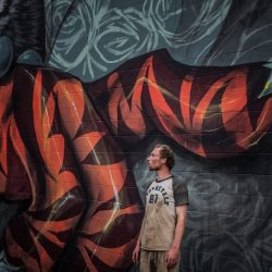 An image of a man standing in front of a mural